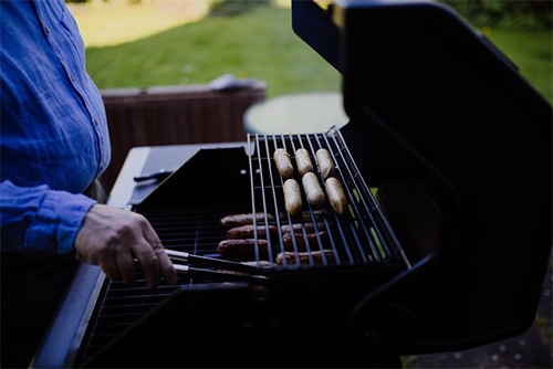 man grilling sausages on a gas grill