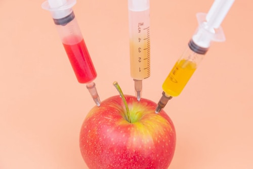 Syringes with different chemicals injections into a red apple