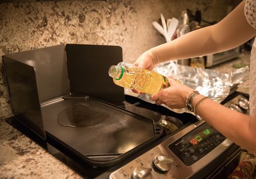 Woman pouring cooking oil onto stove top griddle