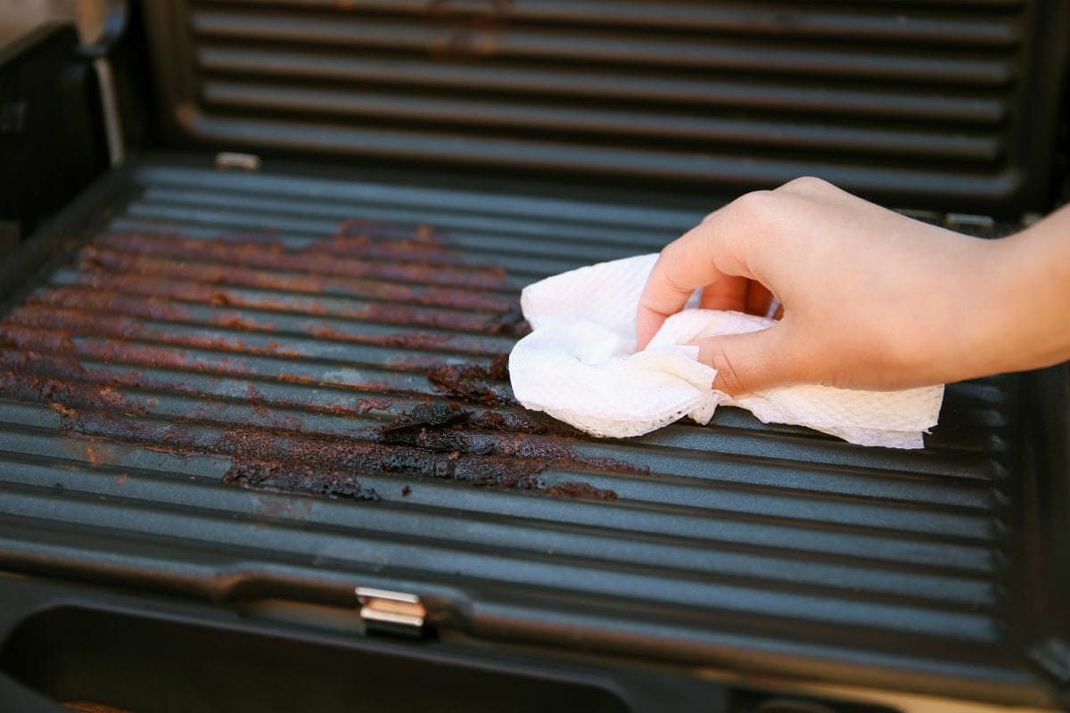 Female Hand Cleaning a Dirty Grill with a Piece of Cloth